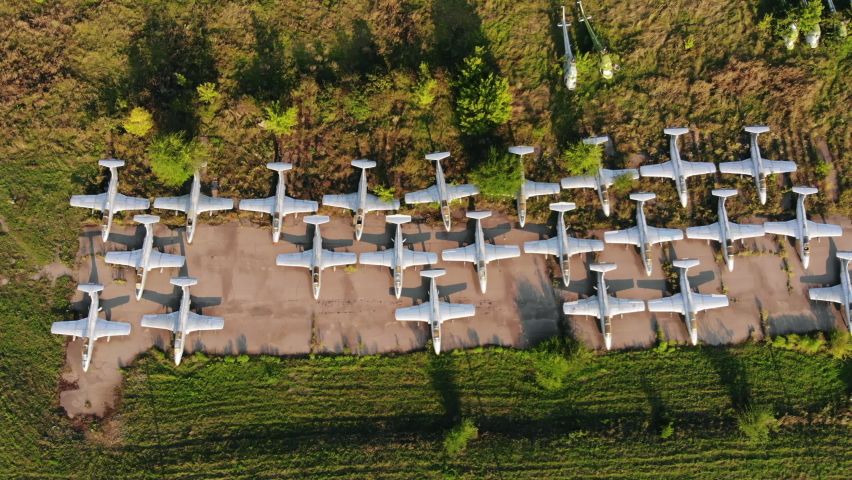 Squadron of old jet fighters used by USSR army stands near dismantled MI-8 helicopters on ground at abandoned air base upper view