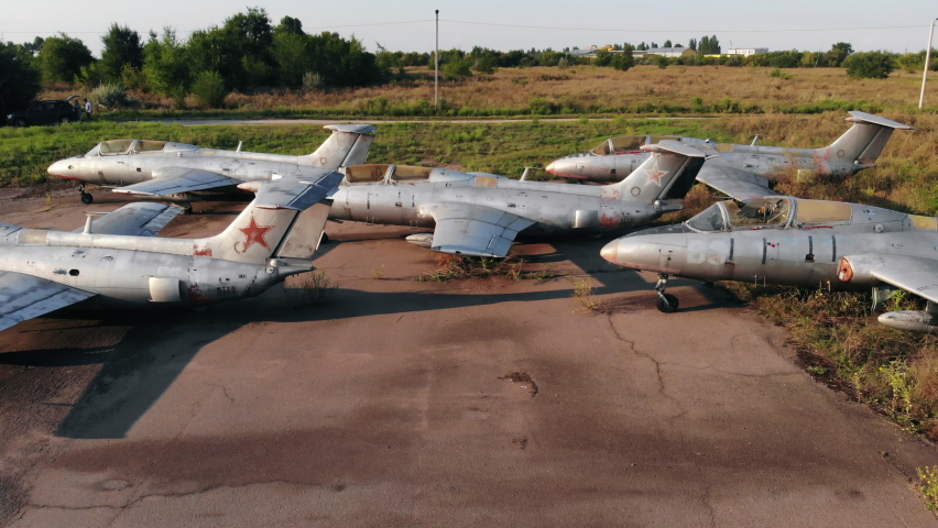 Group of ancient jet warplanes with grey fuselages used by USSR army stands on ground at abandoned air base at sunset aerial view