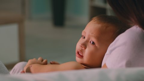 Unhappy toddler rolling on lap of crop mother and crying while resting on sofa at home together