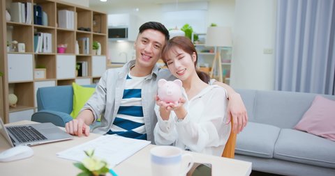 bonding asian couple holding pink piggy bank happily at home