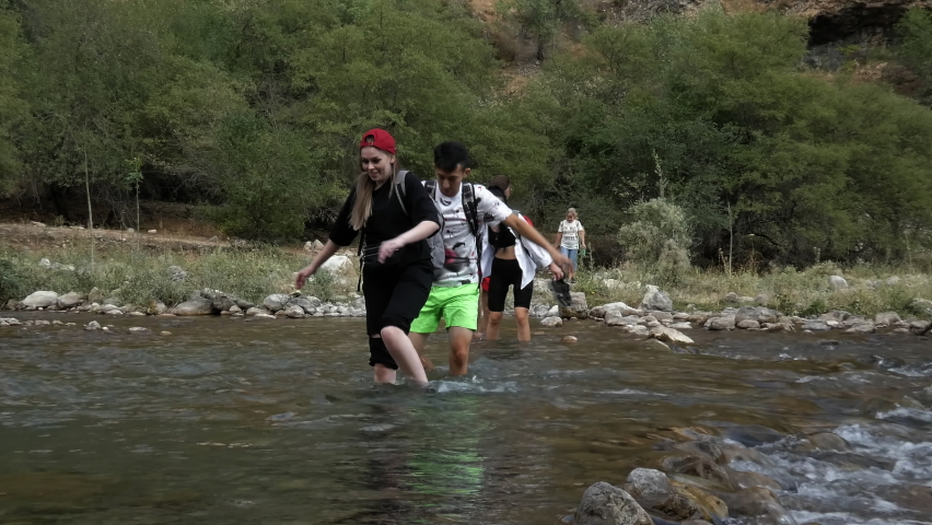 the young white tourists cross the mountain river on the rocky