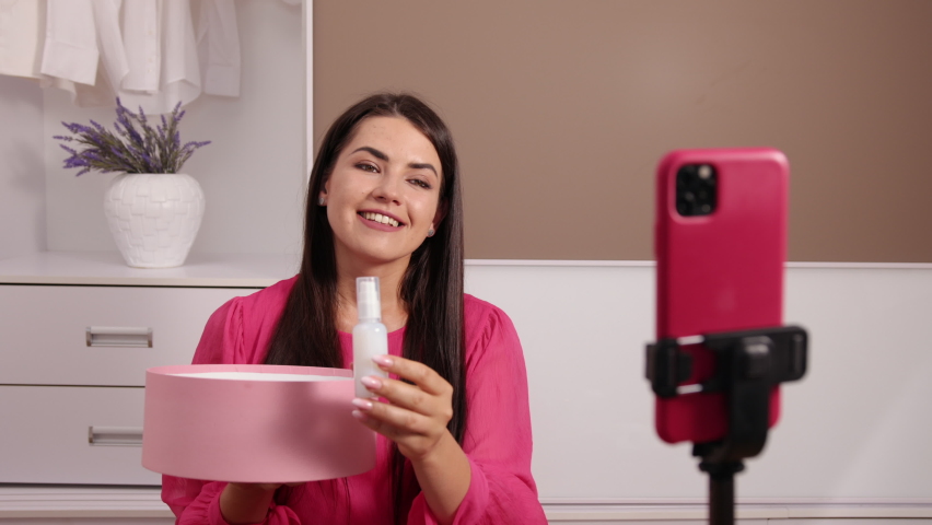 Recording video for beauty blog on camera at home, female influencer shooting brand advertising promo, beautiful young female blogger, stylist sitting in front of smartphone web camera on stabilizer