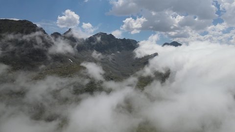 Impressive view of steep rocky mountains and alpine meadows through clouds and fog.