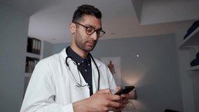 Mixed race male doctor standing in office wearing stethoscope typing on digital device