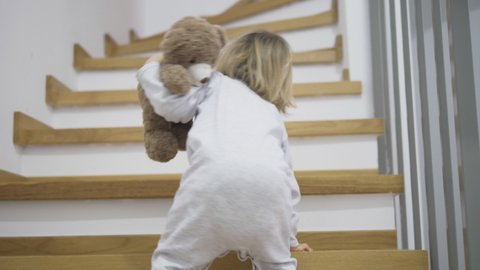 amusing baby child holding a teddy bear toy friend climbing up stairs home, crawling kid