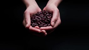 Falling red beans from hands on black background. Shooting of haricots, cereal and groats in studio. Macro footage of pouring out the grits. Food cooking video. 