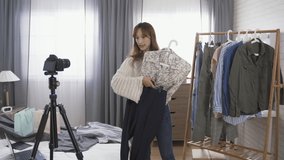 asian blogger recording dresscode guide video at home is hanging formal pants and picking jeans from rack while showing different dressing style with the blouse
