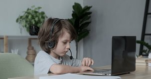 Serious focused boy preschooler learning online through video chat on a laptop. Child studying computer work, typing, and coding. A kid gamer is streaming and playing a video game.