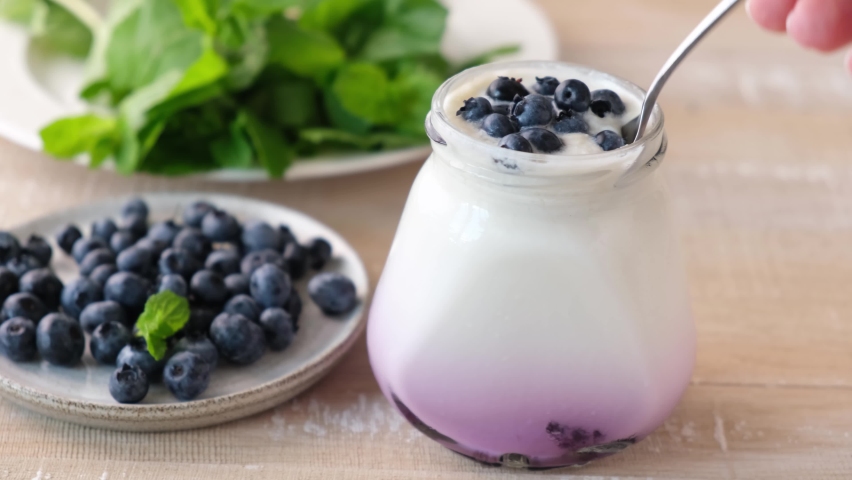 Yogurt with blueberries in glass jar. Taking spoonful of natural greek yogurt | Shutterstock HD Video #1079236340