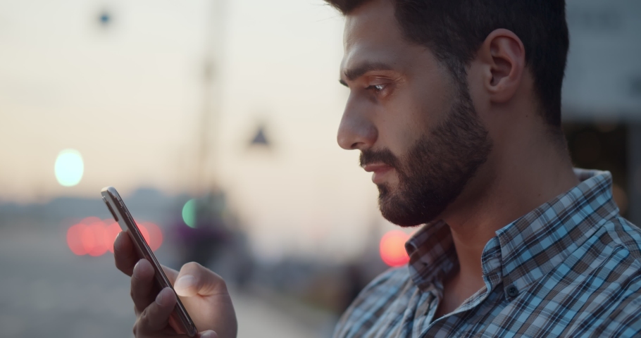 Bokeh close up shot of indian man using smartphone on city street. Handsome guy standing outdoor and checking email on digital gadget | Shutterstock HD Video #1079238692