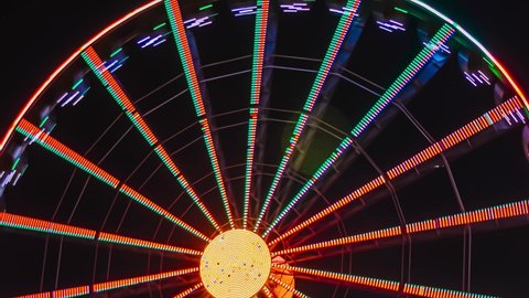 Timelapse of a rotating Ferris wheel glowing with multicolored lights on a long shutter speed in the evening in an amusement park, psychedelic abstract video