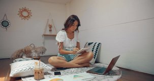 Cute woman seats in lotus pose and doing freelance work at home in cozy place upstairs the house
