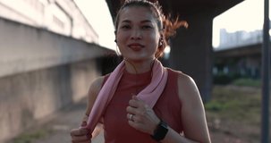 Slow motion video, woman runner wear earphones running in urban park with sunlight from back as rim lighting. Sport female workout in the orange evening light.