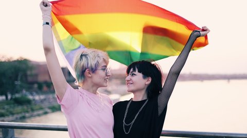 Happy non-binary couple waving rainbow flag
