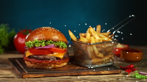 Super Slow Motion Shot of Fast Food Concept. Falling French Fries on Wooden Cutting Board next to the Fresh Hamburger at 1000fps.