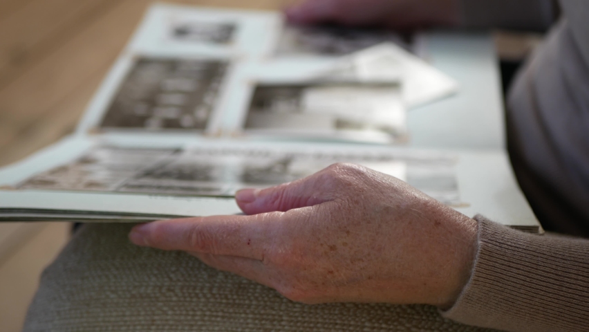 Adult woman looks old photo album at home. Close up view of aged woman
