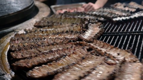 Many chopped pieces of pork ribs grilling on a rotating circle wire rack moving around in a restaurant. Video background.