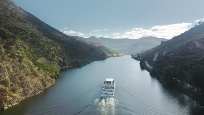 Aerial shot of boat floating in picturesque mountains landscape, Peso da Regua, Vila Real, Portugal, Europe. Birds eye view of Douro river surrounded agricultural area of grape plants, 4k footage Royalty-Free Stock Footage #1079261270