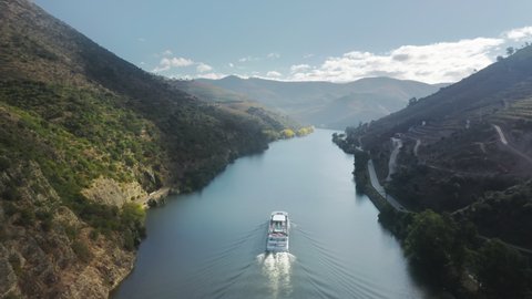 Aerial shot of boat floating in picturesque mountains landscape, Peso da Regua, Vila Real, Portugal, Europe. Birds eye view of Douro river surrounded agricultural area of grape plants, 4k footage
