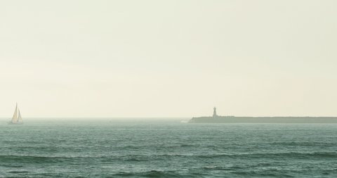 Sailboat Sailing Across The Atlantic Ocean With Lighthouse In Figueira da Foz Foreshore In Portugal. Wide Shot