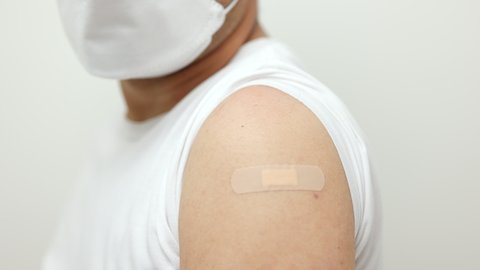 Young asian man wearing mask feel pain in arm after receiving the vaccine. He was worried and stressed that there would be side effects. He tried to massage his aching arm.