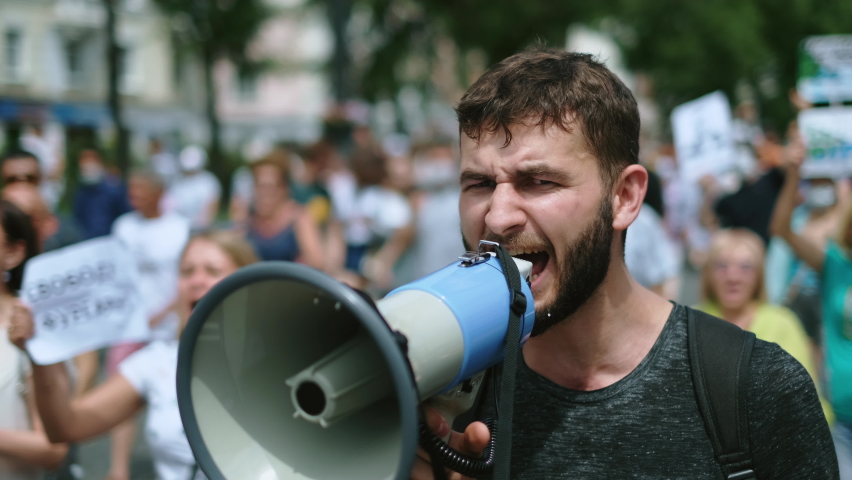 Angry political protester guy with bullhorn marches in protest crowd. Male rebel speaking on demonstration revolt resistance. Strike activist demonstrator man on opposition rally riot with megaphone. Royalty-Free Stock Footage #1079272706