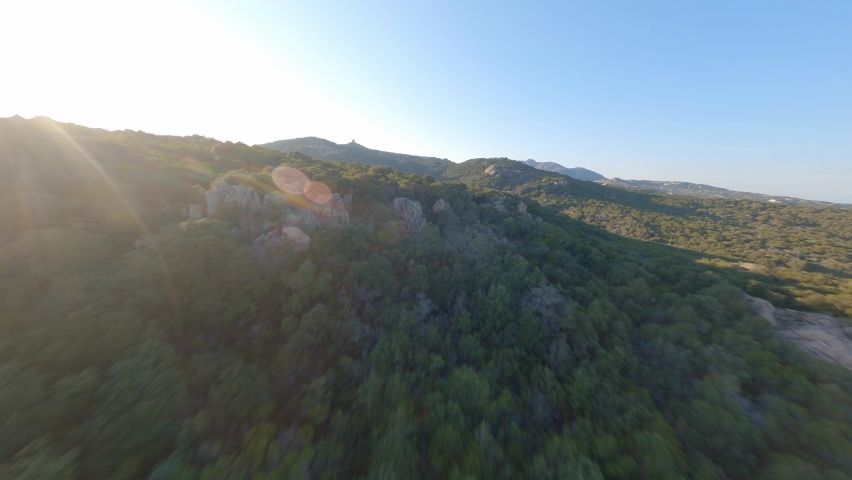 FPV video, view from above, aerial view from an FPV drone flying at high speed over some mountains and green hills with a beautiful sea in the distance. Liscia Ruja, Costa Smeralda, Sardinia, Italy. Royalty-Free Stock Footage #1079273306