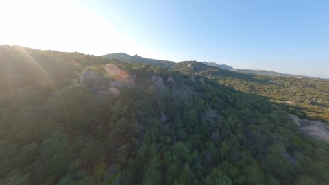 FPV video, view from above, aerial view from an FPV drone flying at high speed over some mountains and green hills with a beautiful sea in the distance. Liscia Ruja, Costa Smeralda, Sardinia, Italy.