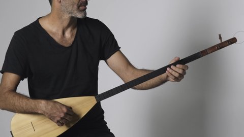 Middle eastern man playing Kopuz which is a string instrument named Baglama with three strings on a white background.
