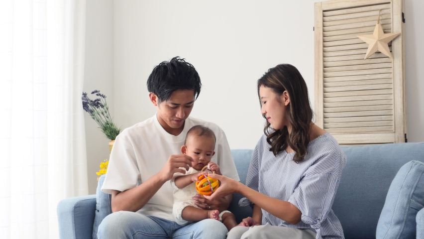 Asian parents sitting down on the sofa with their baby Royalty-Free Stock Footage #1079276885