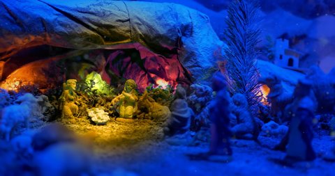 Christmas Nativity Scene with hand-coloured figures in a winter landscape. A magical night atmosphere with colored lights and falling snow.