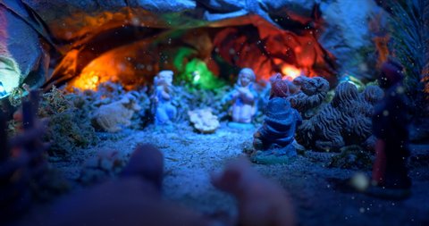 Christmas Nativity Scene with hand-coloured figures, close up of the holy family in a cave. A magical night atmosphere with colored lights and falling snow.