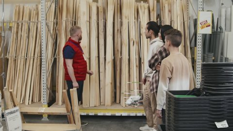 Slowmo shot of male hardware store employee showing wood plank to family of three and giving them advice