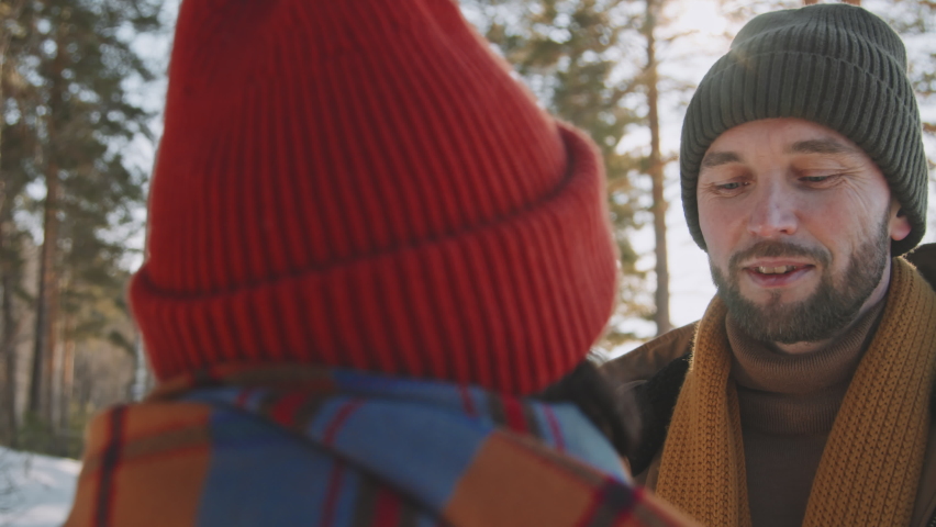 Handheld close up of caring woman and happy man wearing warm chatting while on date in forest on sunny winter day