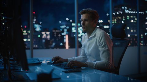 Financial Analyst Working on a Computer with Multi-Monitor Workstation with Real-Time Stocks, Commodities and Exchange Market Charts. Businessman Works in Investment Bank Downtown Office at Night.