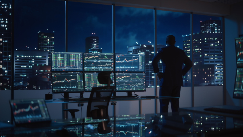 Successful Businessman Looking Out of the Window on Late Evening. Modern Hedge Fund Office with Computer with Multi-Monitor Workstation with Real-Time Stocks, Commodities and Exchange Market Charts. | Shutterstock HD Video #1079285528