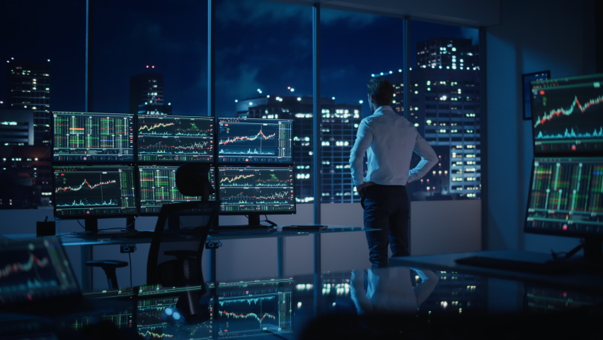 Successful Businessman Looking Out of the Window on Late Evening. Modern Hedge Fund Office with Computer with Multi-Monitor Workstation with Real-Time Stocks, Commodities and Exchange Market Charts. Royalty-Free Stock Footage #1079285564