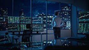 Successful Businessman Looking Out of the Window on Late Evening. Modern Hedge Fund Office with Computer with Multi-Monitor Workstation with Real-Time Stocks, Commodities and Exchange Market Charts. - Powered by Shutterstock - Get 15% off with code: PIKWIZARD15