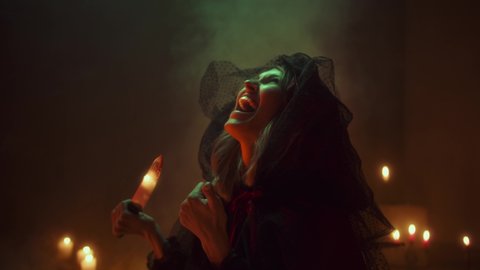 Witch woman cutting finger with knife for sacrifices, sitting in pentagram circle. Sorceress making rite at night, using blood and black witchcraft, cow skull, candles on floor. Halloween concept.