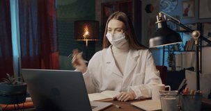 Young woman wearing protective mask, female intern working at night in uniform with a computer in a medical office. Doctor nurse using laptop computer and video call, overtime at the workplace.