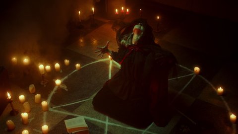Crazy witch woman sitting in pentagram circle and reading spell. Evil sorceress making rite and sacrifices at night, using black witchcraft, cow skull and candles on floor, shouting. Halloween time.