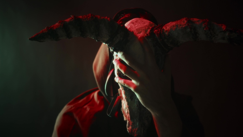Man exorcist putting on cow skull mask close-up. Creepy devil costume with horns, preparing for making rite, black magic and witchcraft. Full moon and Halloween concept. Day of The Dead. | Shutterstock HD Video #1079287760