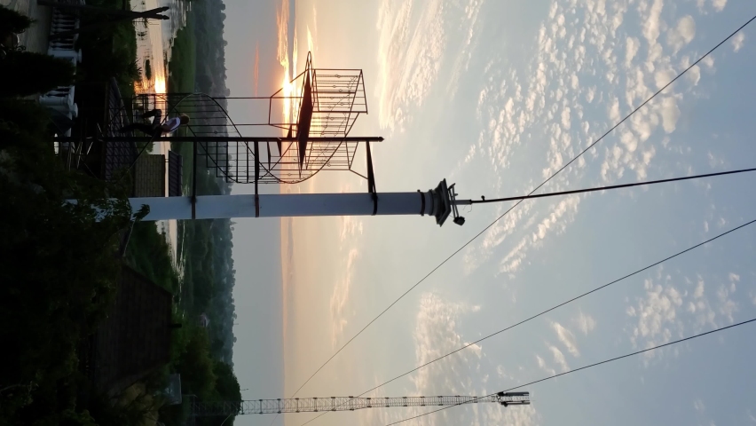 Timelapse landscape with clouds in sunset sky and pillar near winding stair of panoramic view. Unrecognizable person silhouette climbing and walking down by stairs. Vertical format time lapse