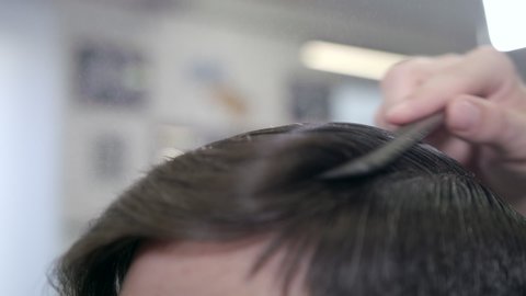 Barber combs his hair to a guy and sprinkles hair on the spray gun. Barber Shop in slow motion, extreme close-up shot.