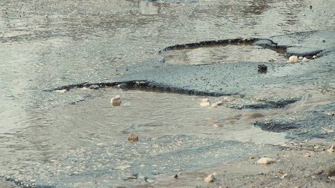 Round potholes on the asphalt, damaged road infrastructure after rain. Cars drive slowly along the road with pits and puddles. Asphalt in violation of technology. Taxpayer money is wasted. UHD 4K.