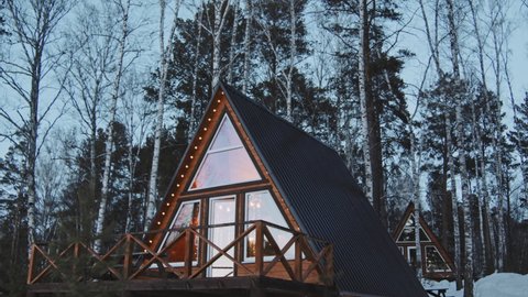 PAN slowmo shot of cozy A-frame cabins in forest on cold winter evening