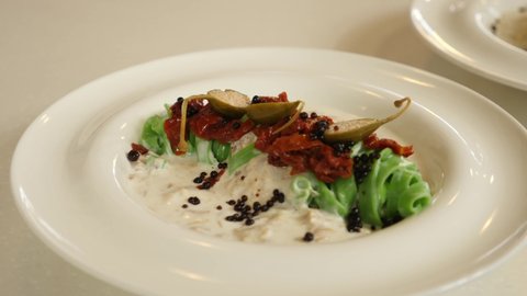 restaurant dish - original serving of green noodles with sun-dried tomatoes and capers in sauce