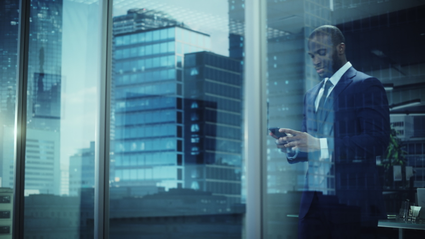 Portrait of Successful Black Businessman Wearing Suit Standing, Using Smartphone Looking out of the Window. Successful African CEO Planning e-Commerce Investment Strategy. From Outside Shot Royalty-Free Stock Footage #1079293097