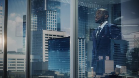 Portrait of Smiling African-American Businessman in a Suit Standing in His Office and Looking out of the Window on Big City. Successful Investment Manager Working Hard to be on Top. Outside Shot