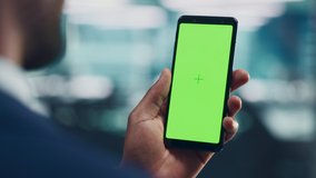 Black Man with Green Screen Chroma Key Smartphone in Office. African-American Person using Internet, Social Media, Online Shopping with Mobile Phone Device. Focus on Display, Hand